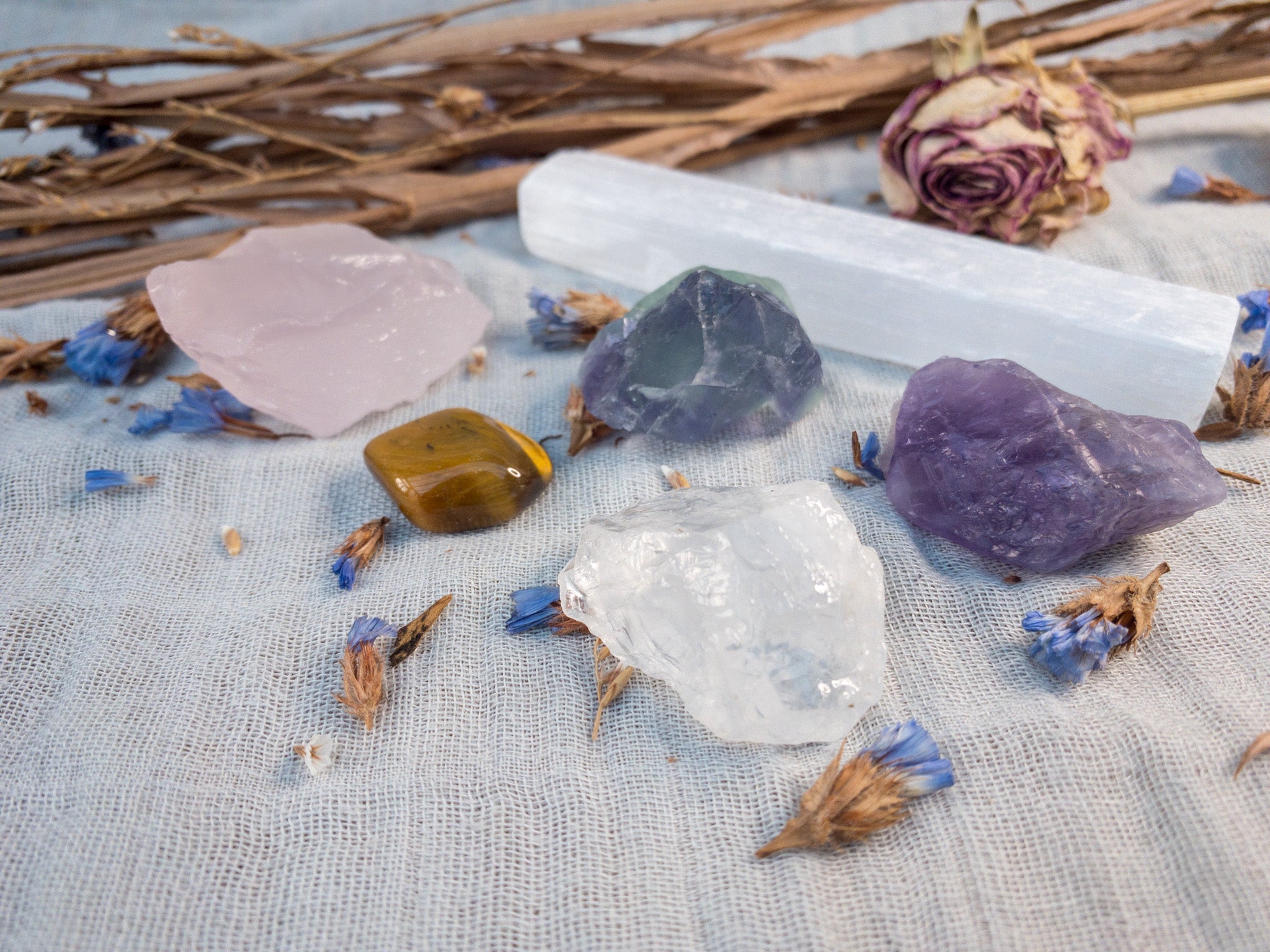 crystal collection with selenite, amethyst, clear quarts, rose quartz, tigers eye, rainbow fluorite on a grey background with dried flowers