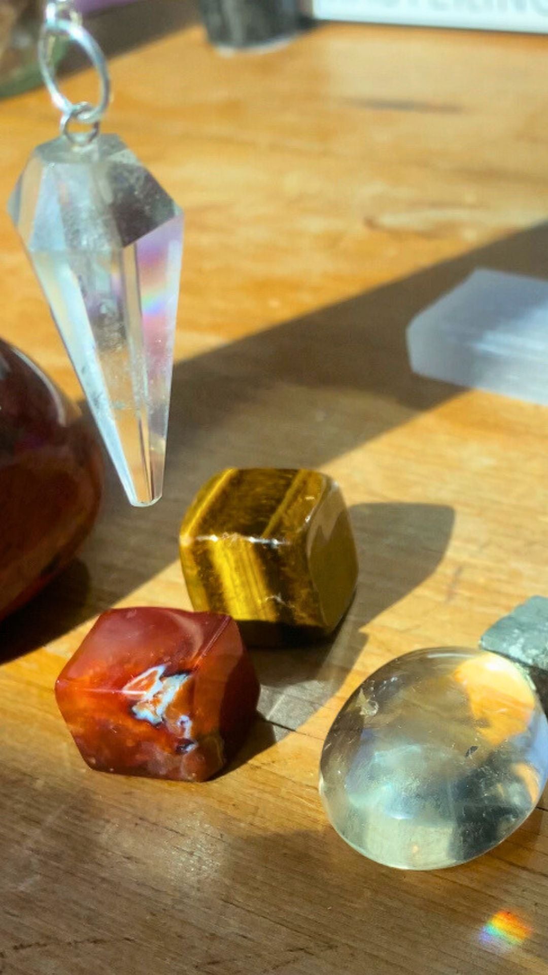 Distance crystal healing, a clear quartz pendant over a carnelian cube, tigers eye cube and citrine on a wooden table