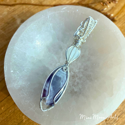 moonstone and amethyst wire wrapped silver wire pendant showing the back of the pendant in a selenite bowl with a wooden table back ground