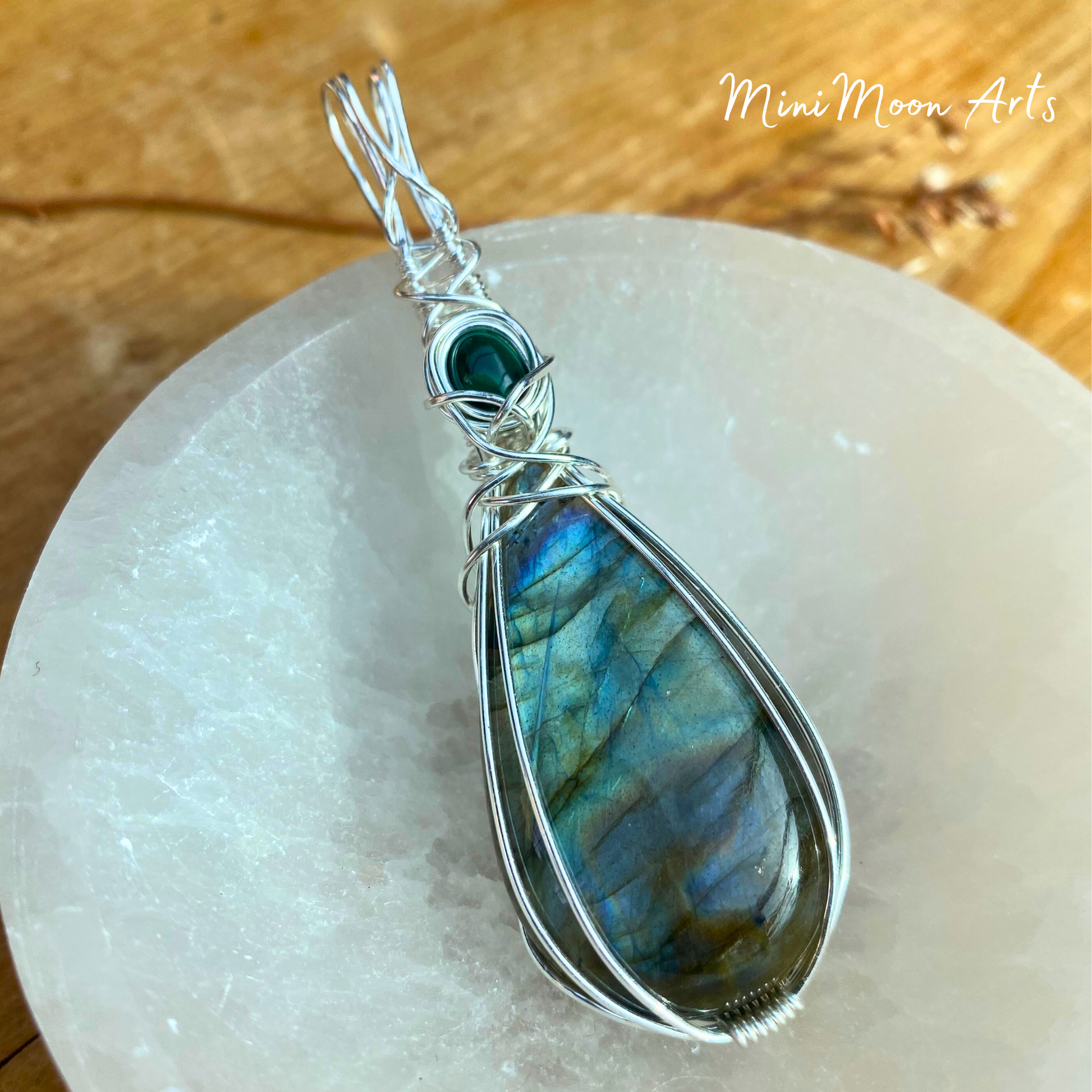 Transform and evolve Labradorite and malachite wire wrapped silver wire pendant sat at a slight angle in a selenite bown and wooden table background