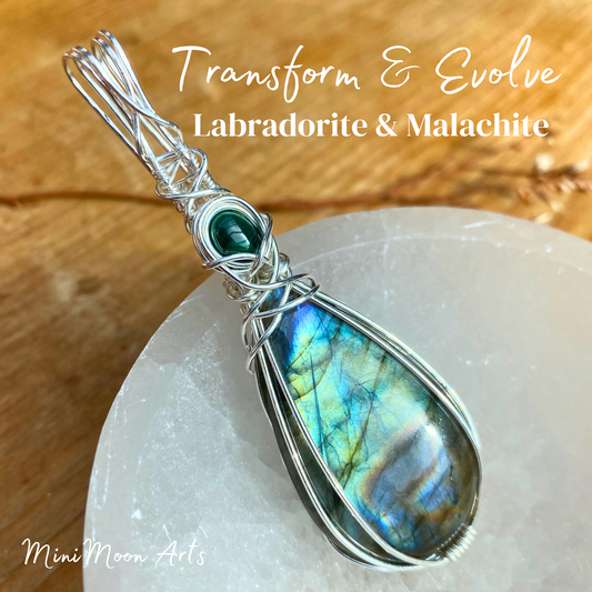 Transform and evolve Labradorite and malachite wire wrapped silver wire pendant sat at an angle in a selenite bown and wooden table background