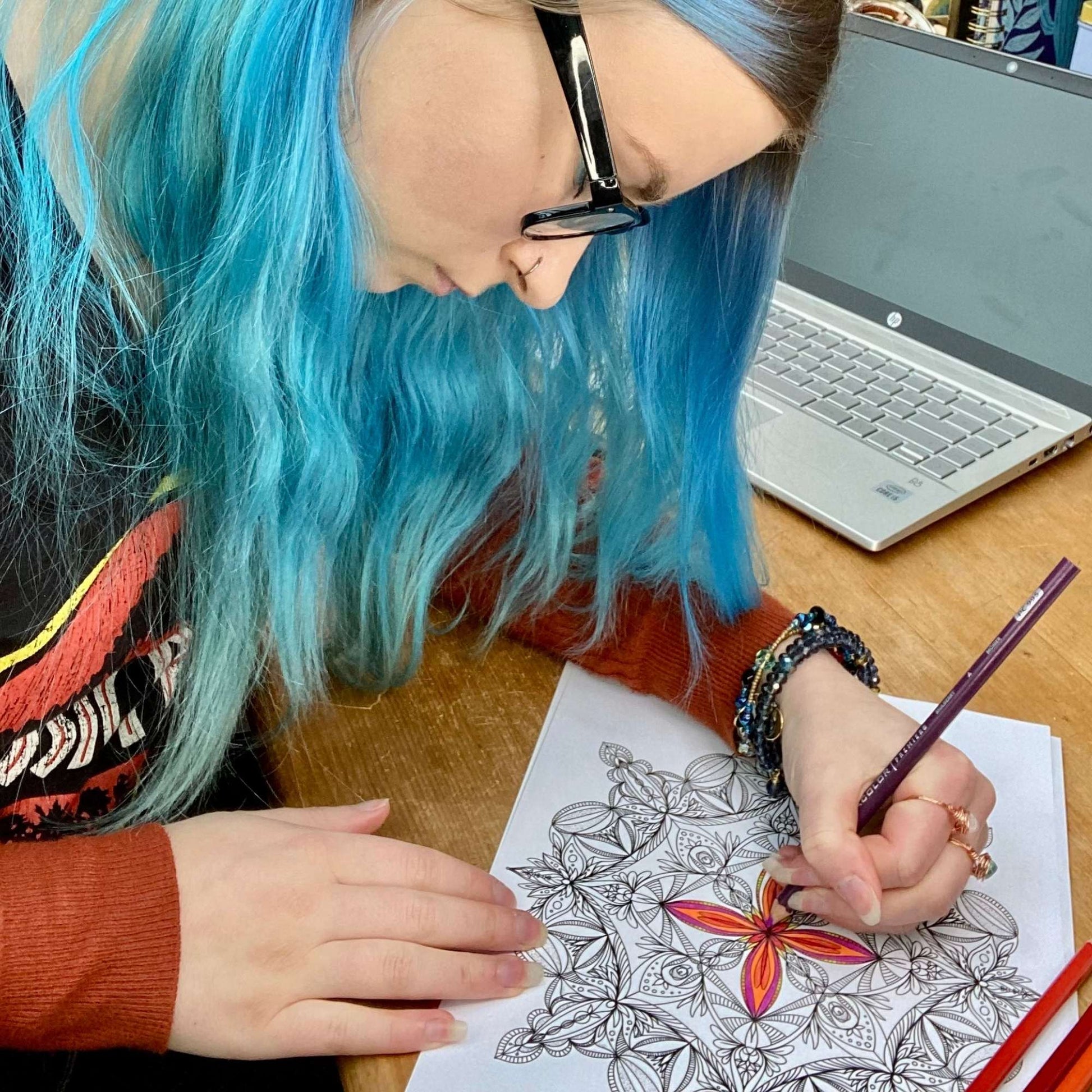 blue haired woman colouring colouring sheet with laptop computer in back groud