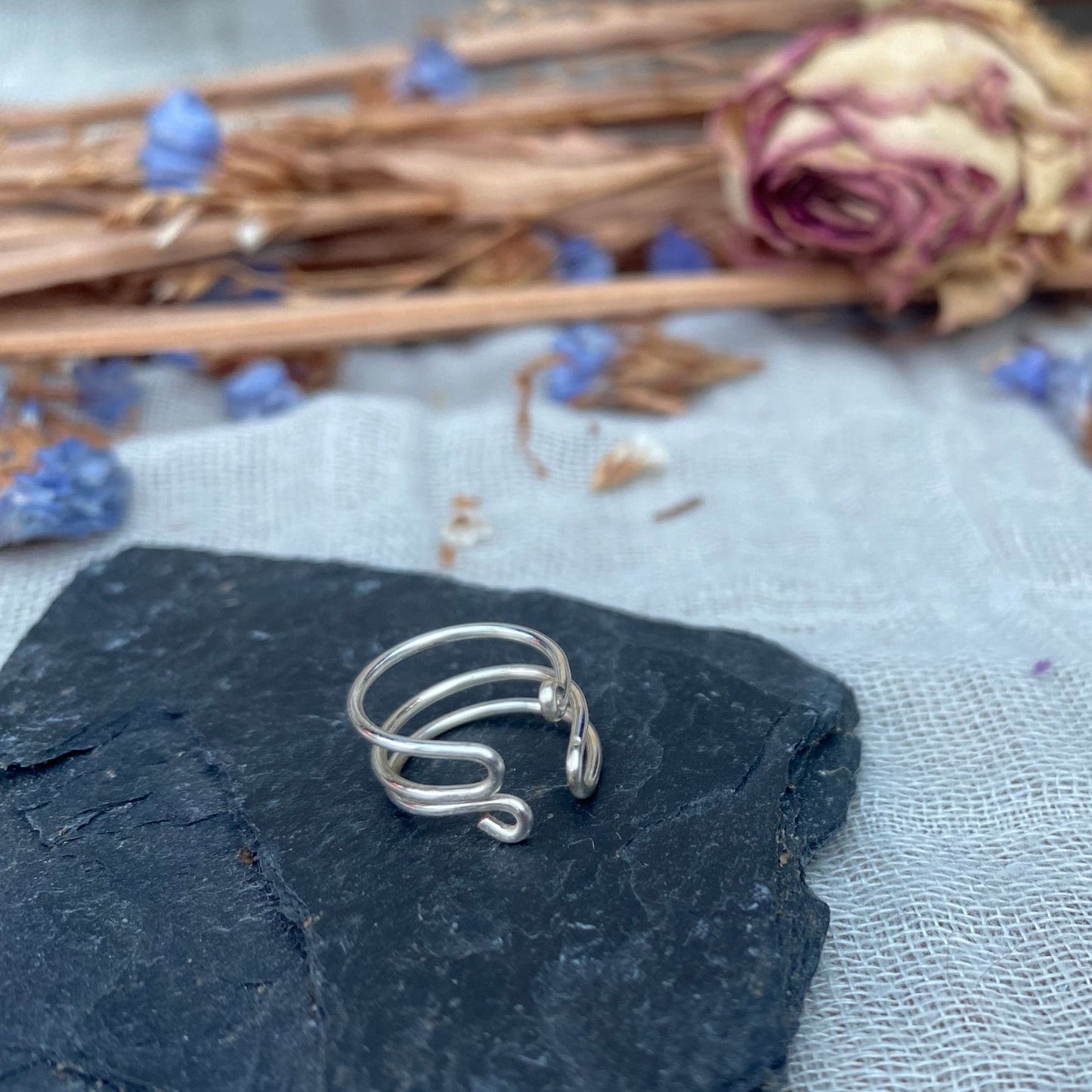 silver adjustable ear cuff sat on a piece of slate with dried rose and purple flowers in back ground